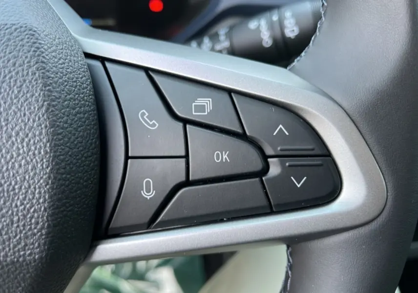 Gros plan sur les commandes noires du volant cuir gris du Dacia Bigster Hybrid 155 Expression Plus, boutons multifonctions visibles.