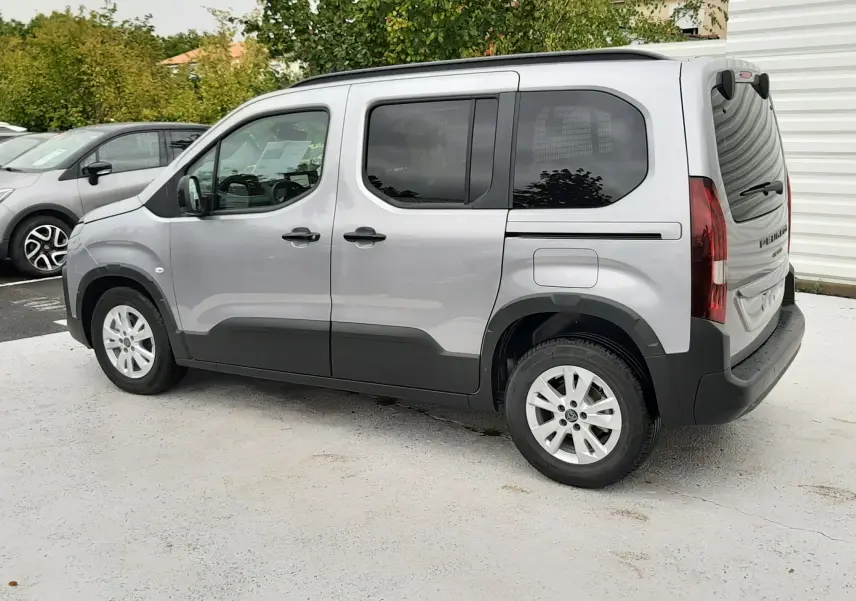 Peugeot Rifter gris acier vu de profil côté gauche, avec vitres arrière surteintées et barres de toit noires.
