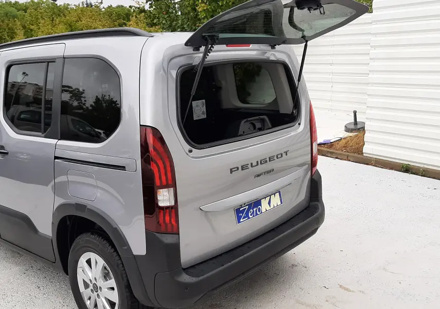 Vue 3/4 arrière droite d’un Peugeot Rifter gris acier 2026 avec hayon ouvert et vitres arrière surteintées.