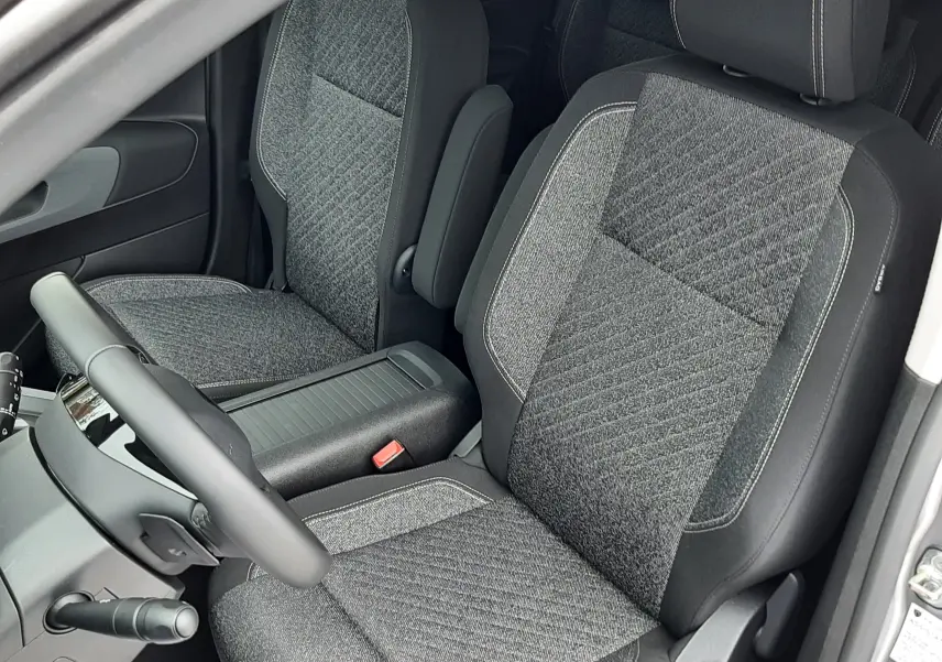 Vue intérieure côté conducteur du Peugeot Rifter gris acier 2026, sièges tissu gris avec coutures contrastées.