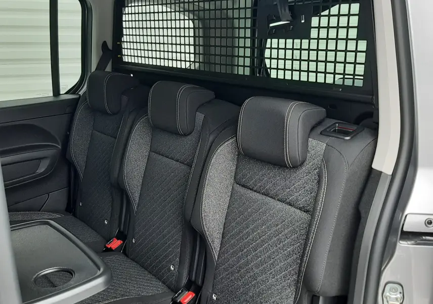 Vue intérieure côté droit du Peugeot Rifter gris acier, montrant les trois sièges individuels arrière avec séparation grillagée.