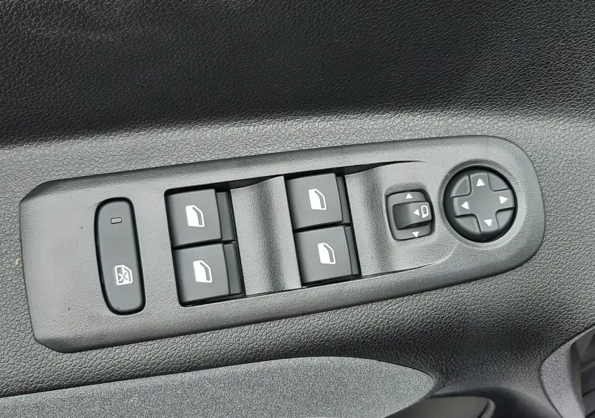 Gros plan sur les commandes électriques des vitres et rétroviseurs sur la porte côté gauche du Peugeot Rifter gris acier 2026.