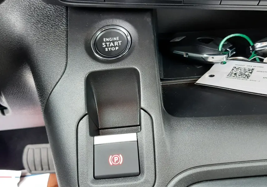 Gros plan intérieur sur la console centrale du Peugeot Rifter gris acier, montrant le bouton start/stop et frein à main électrique.