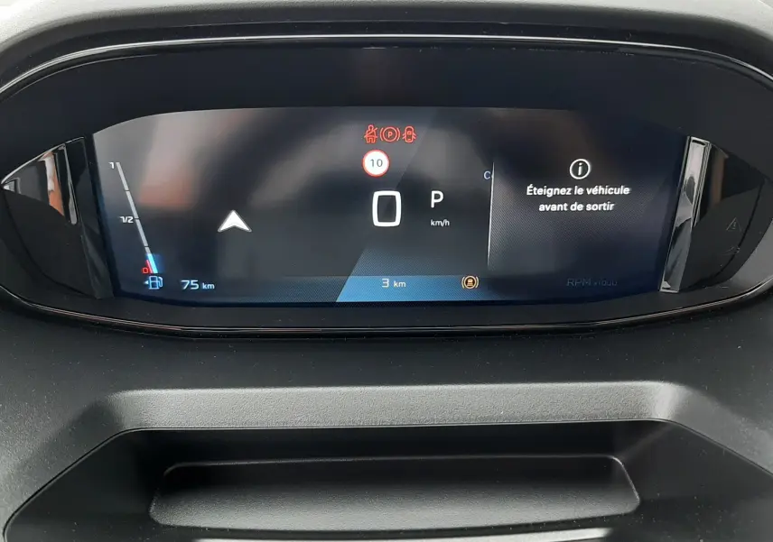 Vue rapprochée du tableau de bord numérique du Peugeot Rifter gris acier, affichant le compteur et un message d'alerte.