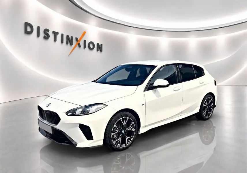 BMW Série 1 blanche vue en 3/4 avant droit, avec jantes alliage noires et calandre M sport dans un showroom lumineux.