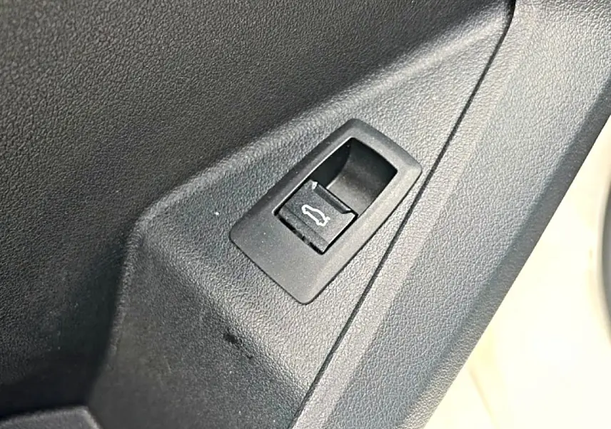 Gros plan sur le bouton d'ouverture du coffre dans l'habitacle d'une BMW Série 1 blanche.