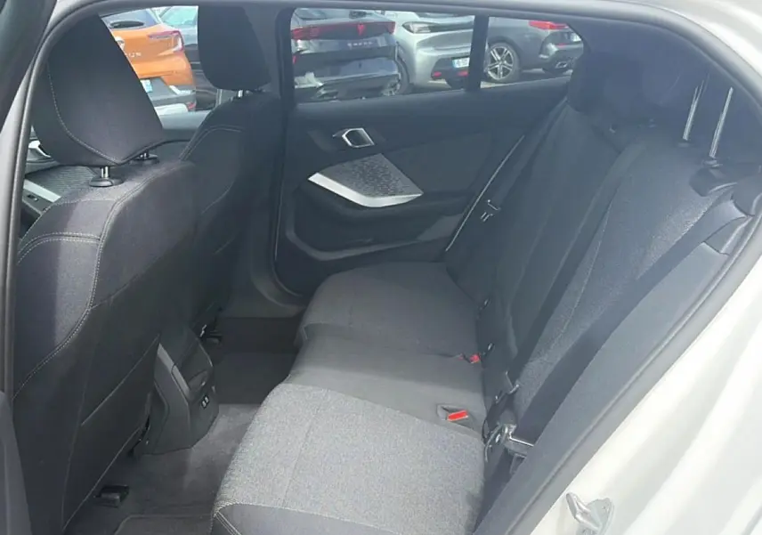 Vue intérieure arrière côté droit de la BMW Série 1 blanche, montrant la banquette tissu gris et les portes ouvertes.