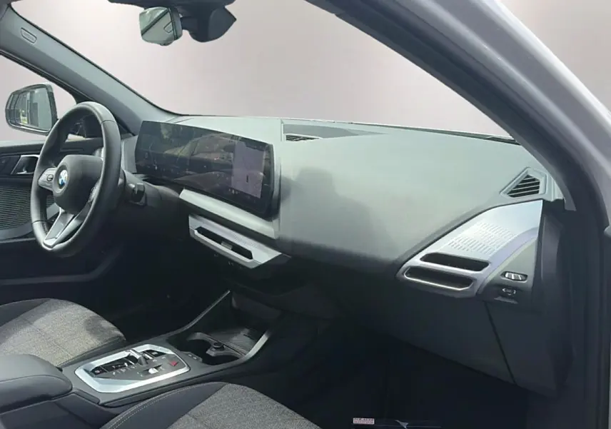 Intérieur de BMW Série 1 120da 2025, vue côté passager, tableau de bord moderne avec écran large et volant cuir.