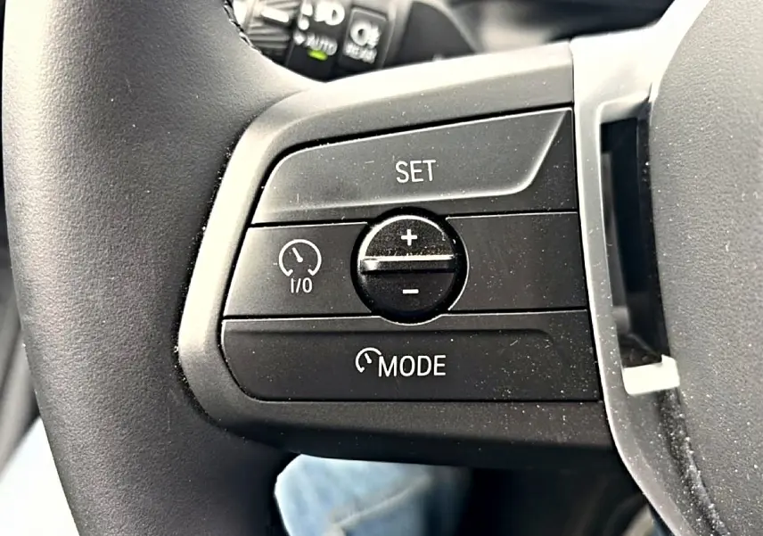 Gros plan sur les commandes de régulateur de vitesse au volant noir de la BMW Série 1 blanche 2025.