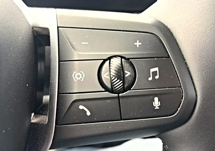 Gros plan sur les commandes noires au volant cuir de la BMW Série 1 blanche, avec boutons de volume et appel.