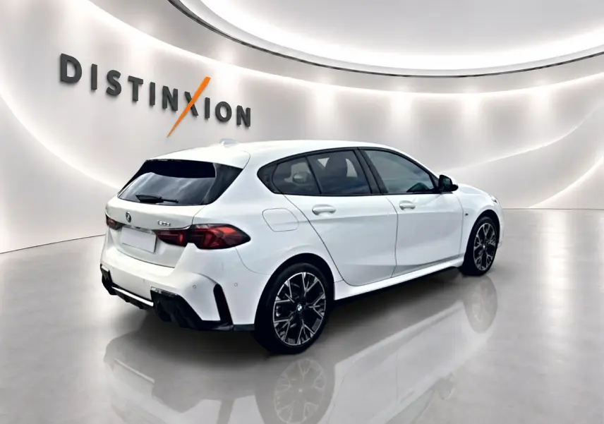 BMW Série 1 blanche vue en 3/4 arrière droit, avec jantes sport noires et détails M Sport visibles.