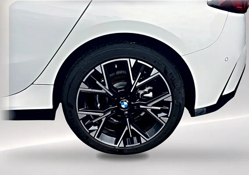 Gros plan sur la roue arrière droite noire et argentée d’une BMW Série 1 blanche pure, avec partie arrière visible.