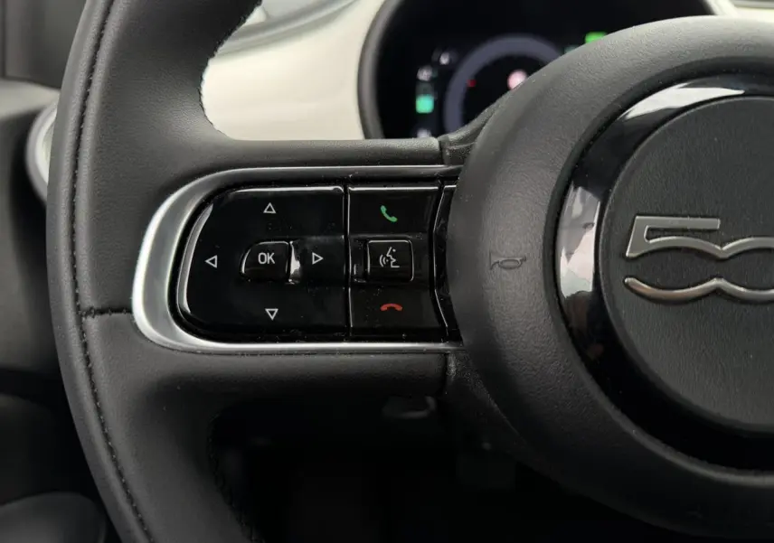 Gros plan sur le volant noir Soft-Touch du Fiat 500 électrique 2024 avec commandes intégrées et logo 500 central.