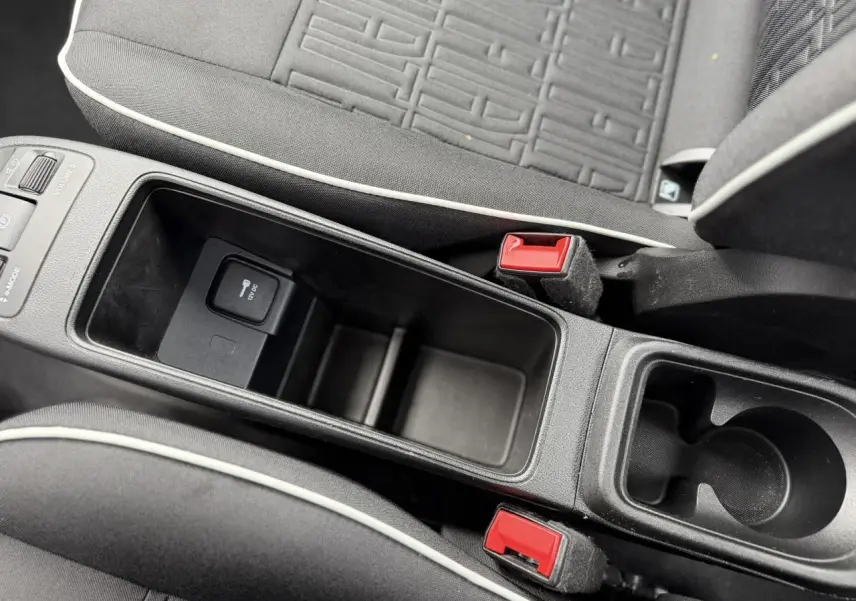 Vue rapprochée de la console centrale noire avec rangement, bouton 12V et sièges tissu noir à surpiqûres blanches dans une Fiat 500 électrique.