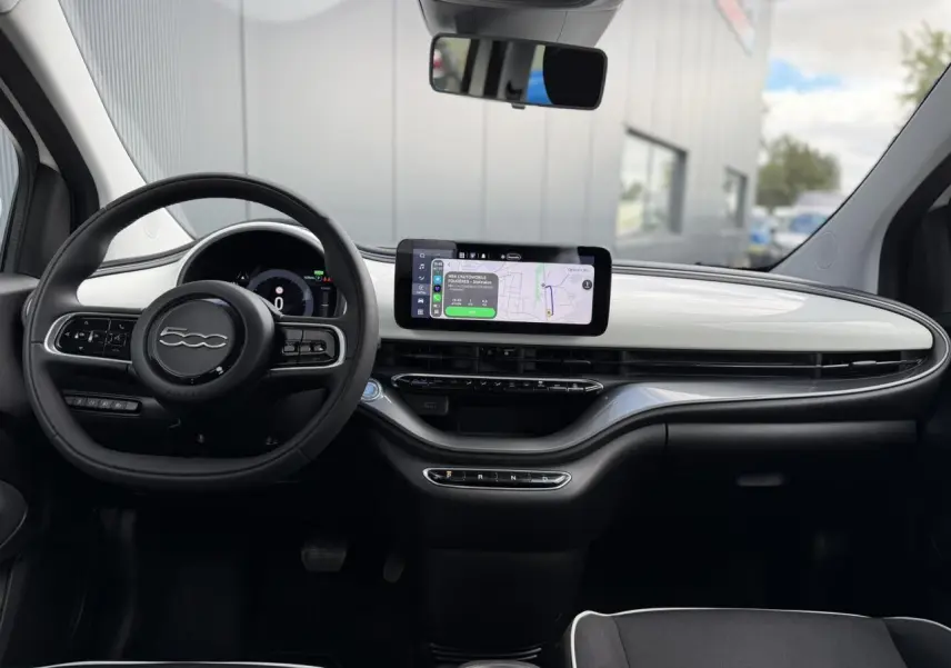 Vue intérieure avant de la Fiat 500 électrique 2024 avec tableau de bord blanc Artic et écran tactile central allumé.