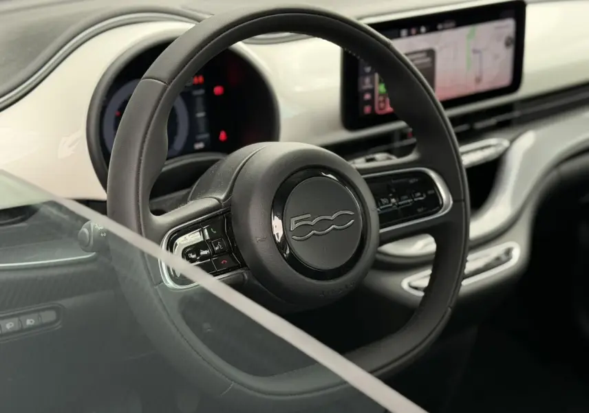 Vue rapprochée du volant noir Soft-Touch et du tableau de bord blanc Artic avec écran tactile du Fiat 500 électrique 2024.