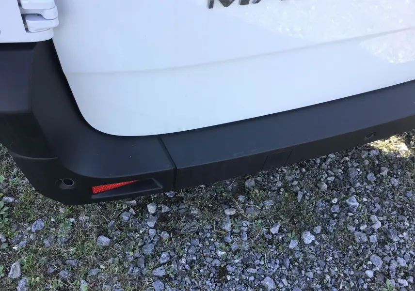 Gros plan sur le pare-chocs arrière gauche blanc du Renault Master L3H2 2025 avec feu réfléchissant rouge et sol caillouteux.