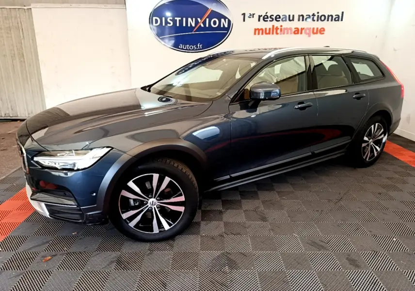 Volvo V90 Cross Country bleu en 3/4 avant droit, avec jantes alliage et rails de toit chromés visibles.