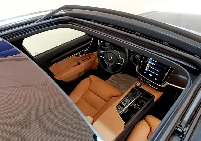 Vue intérieure par le toit ouvrant d'une Volvo V90 Cross Country 2019, sièges cuir marron et tableau de bord moderne noir.