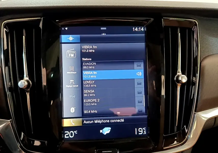 Écran tactile central noir affichant les stations radio dans l’habitacle d’un Volvo V90 Cross Country bleu.