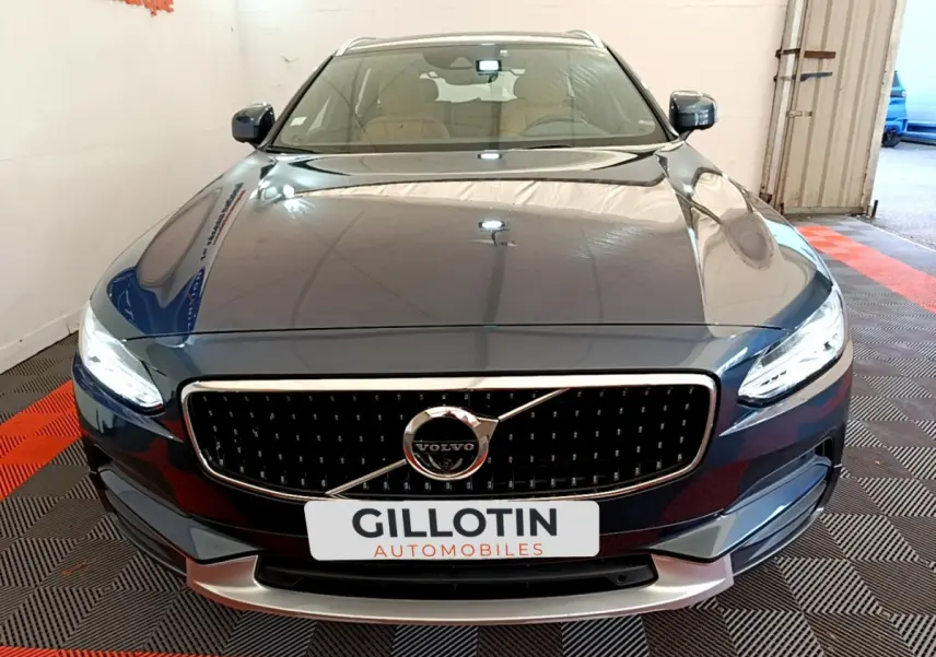 Vue avant d'un Volvo V90 Cross Country bleu avec calandre noire et phares LED allumés dans un garage.