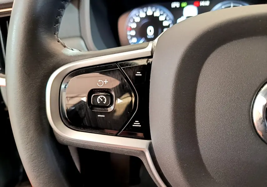 Gros plan sur les commandes gauche du volant noir du Volvo V90 Cross Country 2019 avec tableau de bord numérique en arrière-plan.