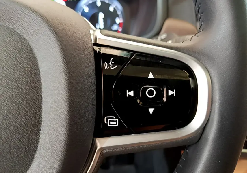 Gros plan sur les commandes vocales et de navigation intégrées au volant en cuir noir du Volvo V90 Cross Country.