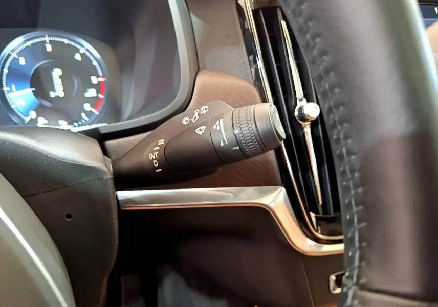 Gros plan sur la manette d’essuie-glace côté gauche du tableau de bord bois et chrome du Volvo V90 Cross Country bleu 2019.