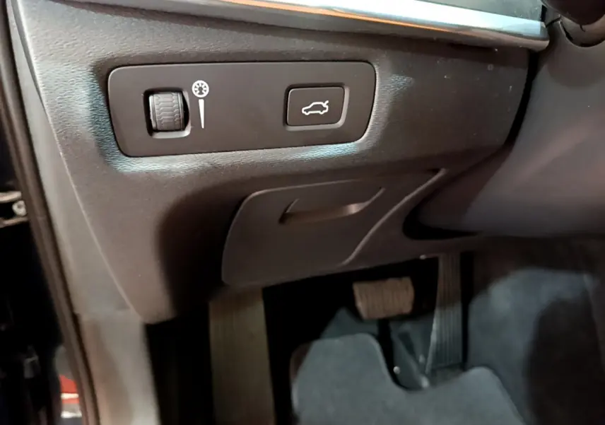 Gros plan sur les commandes sous le tableau de bord côté conducteur du Volvo V90 Cross Country bleu, bouton ouverture coffre visible.