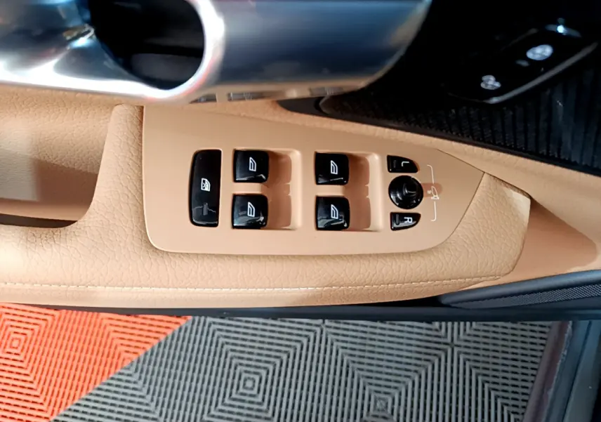 Gros plan sur les commandes des vitres et rétroviseurs sur la porte beige côté conducteur d’un Volvo V90 Cross Country.