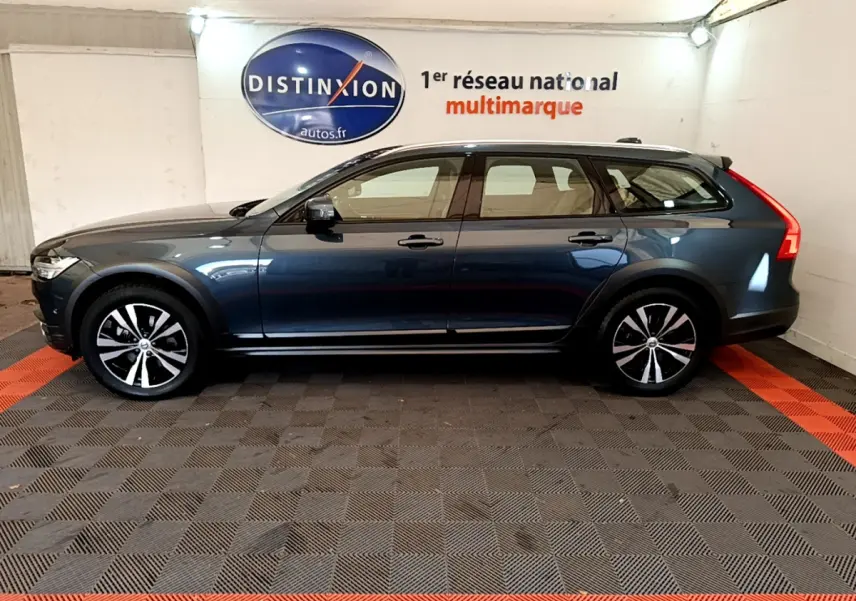 Vue de profil côté gauche d’un Volvo V90 Cross Country bleu dans un showroom avec sol à damier noir et rouge.