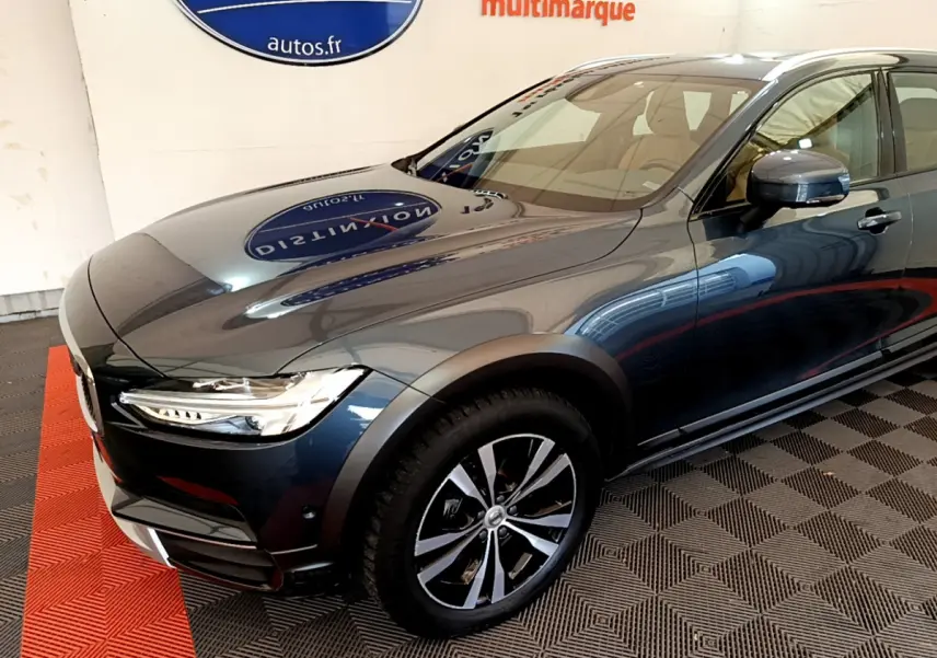 Vue 3/4 avant droit d'un Volvo V90 Cross Country bleu métallisé avec jantes alliage et phares LED allumés.