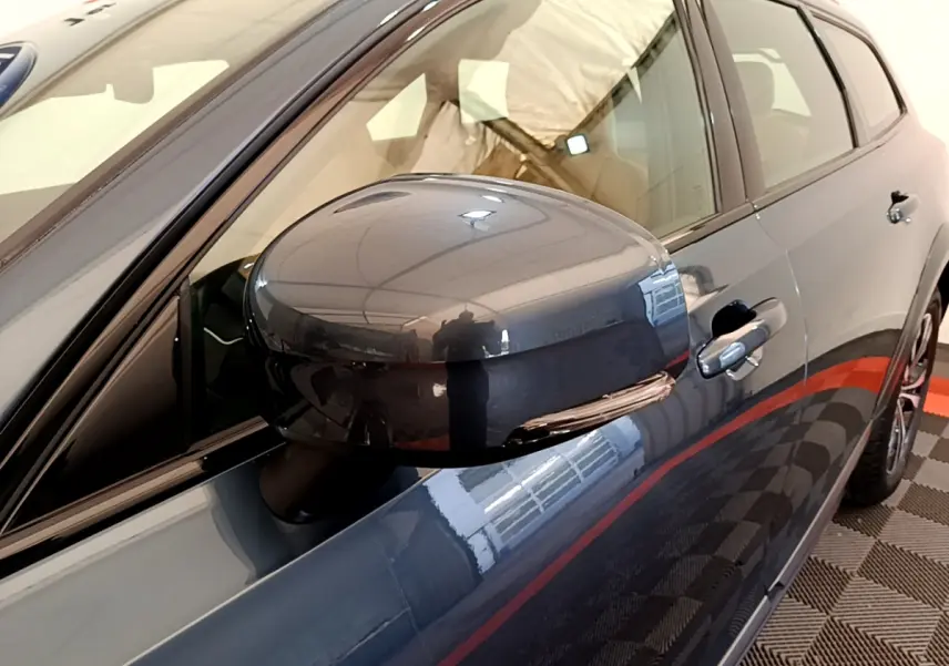 Gros plan sur le rétroviseur côté gauche d’un Volvo V90 Cross Country bleu, avec reflet de l’environnement intérieur.