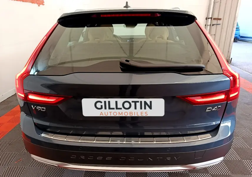 Vue arrière d'un Volvo V90 Cross Country bleu foncé avec feux LED allumés et badge D4 sur un sol à damier.