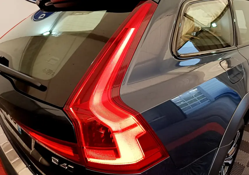 Vue arrière côté droit d'un Volvo V90 Cross Country bleu avec feux arrière LED allumés dans un garage.