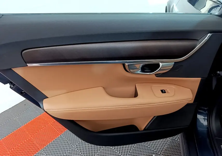 Vue rapprochée de la porte avant gauche beige et noire du Volvo V90 Cross Country bleu, avec poignée chromée.