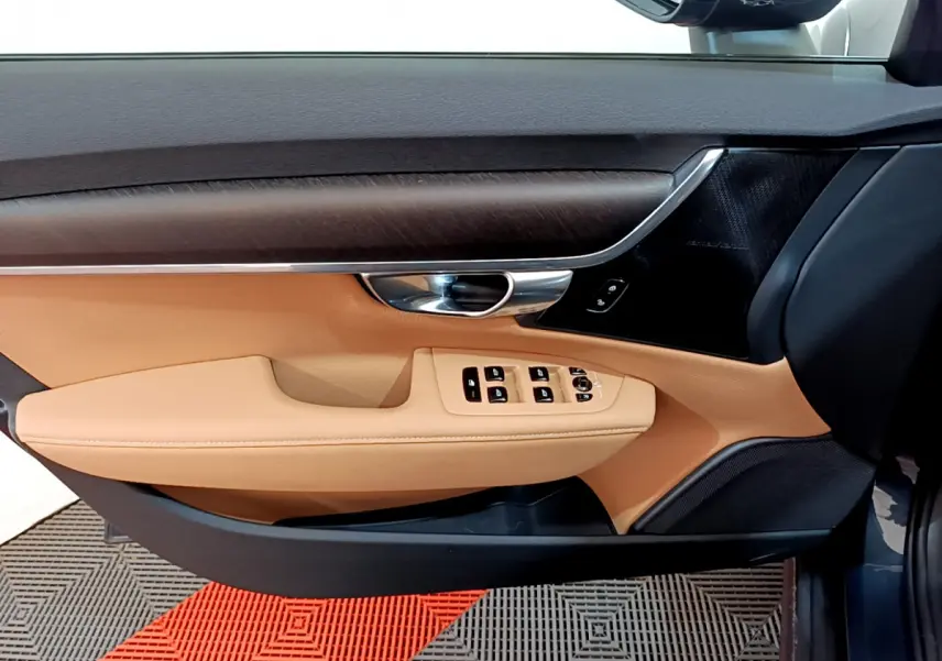 Vue intérieure côté conducteur de la porte beige et noire du Volvo V90 Cross Country bleu avec commandes de vitres et poignée chrome.