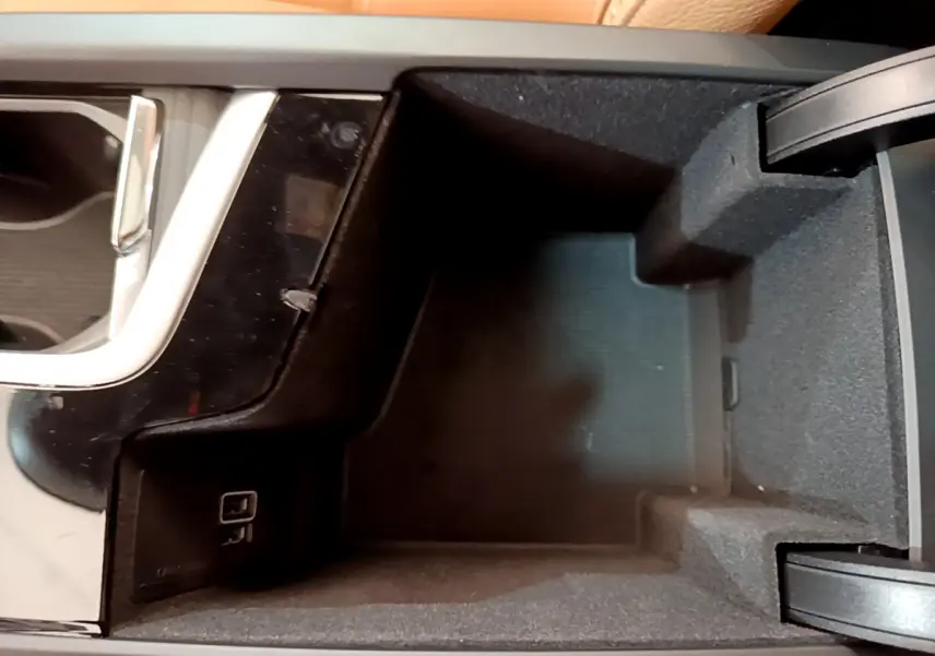 Vue en plongée du rangement central intérieur noir du Volvo V90 Cross Country avec prise USB visible.