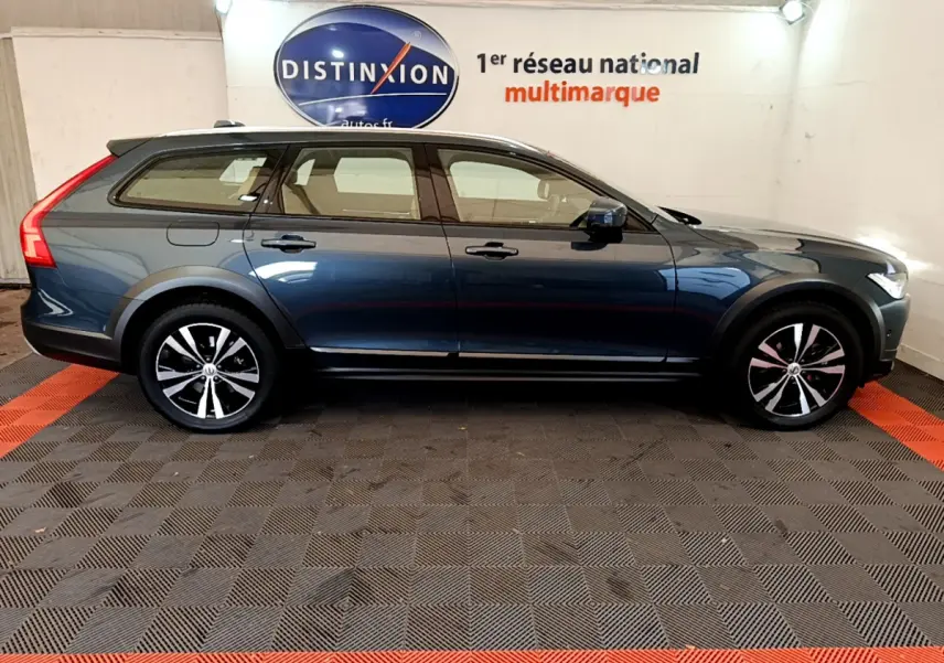 Profil côté gauche d'un Volvo V90 Cross Country bleu 2019, avec jantes noires et toit noir contrasté en intérieur showroom.