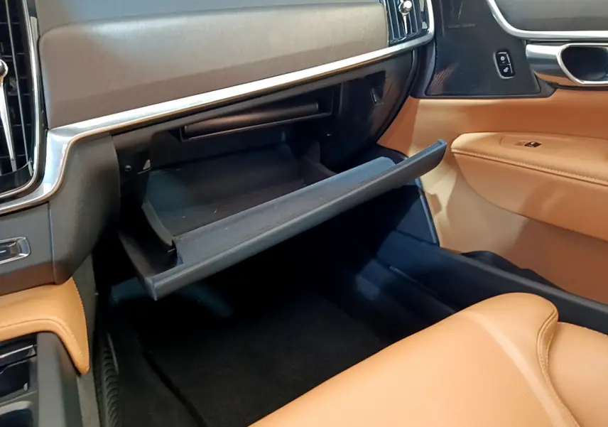 Gros plan sur la boîte à gants ouverte côté passager, intérieur cuir beige et tableau de bord noir du Volvo V90 Cross Country.