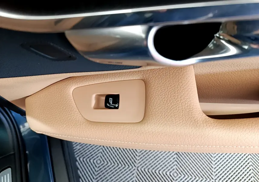 Détail de la poignée intérieure côté gauche en cuir beige avec bouton de fermeture sur Volvo V90 Cross Country bleu.