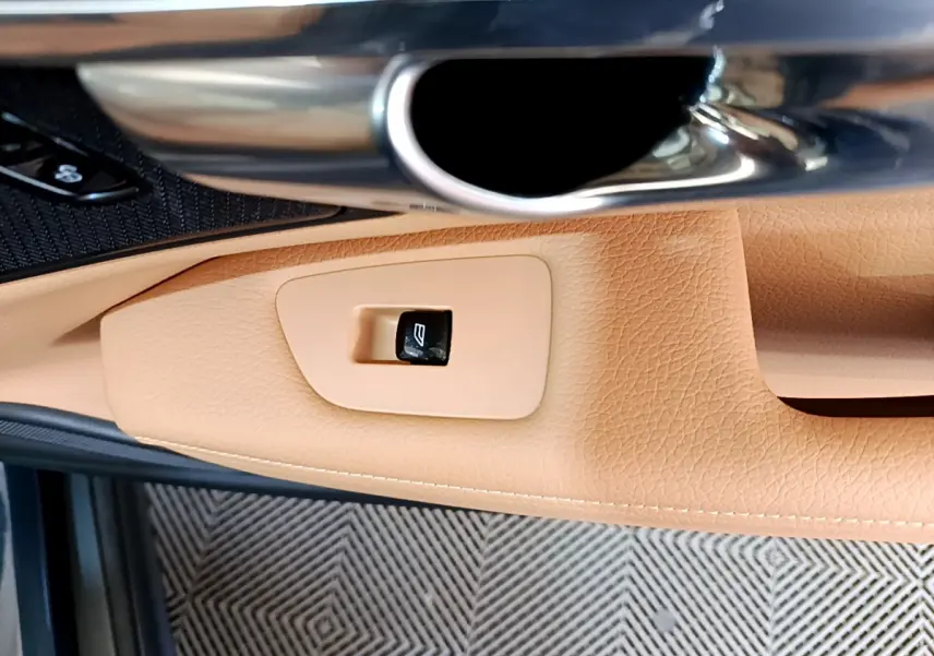 Détail de la poignée intérieure et bouton de lève-vitre en cuir beige du côté gauche d’une Volvo V90 Cross Country bleu.