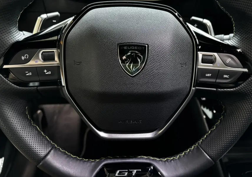 Gros plan sur le volant cuir noir perforé avec logo Peugeot et sigle GT de la 208 Hybrid 136 eDCS6 GT.