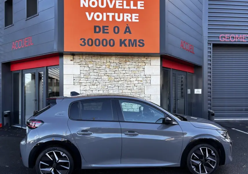 Profil côté droit d'une Peugeot 208 Hybrid 136 eDCS6 GT gris foncé garée devant un bâtiment commercial.