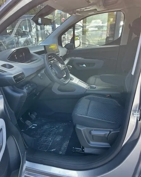 Vue intérieure côté conducteur du Peugeot Rifter gris foncé 2024, avec volant multifonction et tableau de bord digital.