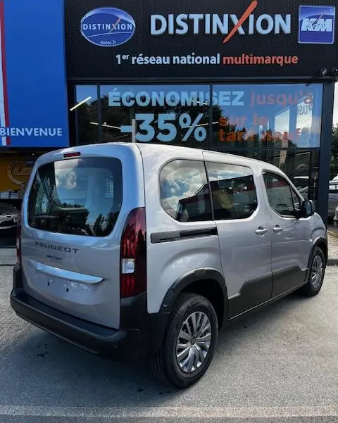 Vue 3/4 arrière droite du Peugeot Rifter gris foncé 2024 avec vitres opaques et rails de toit, stationné devant un concessionnaire.