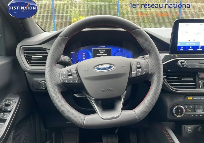Vue intérieure centrée sur le volant perforé du Ford Kuga 2024 avec tableau de bord numérique et écran tactile.
