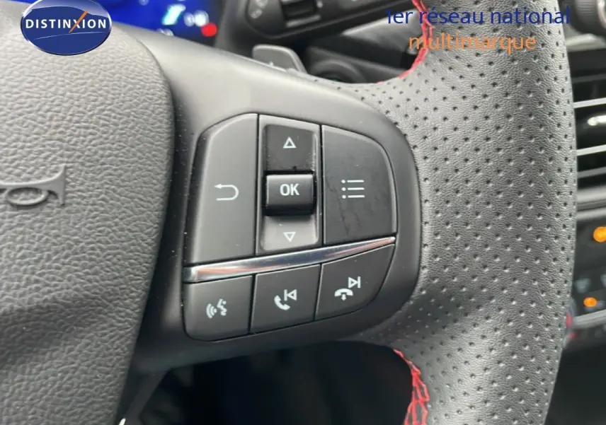Gros plan sur le volant perforé avec surpiqûres rouges du Ford Kuga 2024 bleu Vapor Metal, mettant en valeur les commandes intégrées.