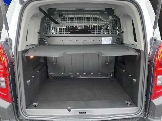 Vue arrière du coffre ouvert d’un Citroën Berlingo blanc 2025 avec séparation grillagée et tablette de rangement.