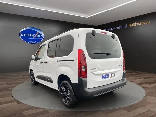 Vue 3/4 arrière droite d'un Citroën Berlingo blanc 2025 avec vitres teintées et jantes noires dans un showroom.